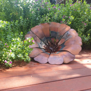 Handcrafted Sun Flower rusted metal art in a garden, featuring a rich orange and red patina, 50 cm diameter.