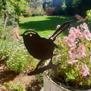 A side view of the Wren Australian Made Rusted Metal garden art, featuring a 22 cm height and rusted patina against a natural garden backdrop.